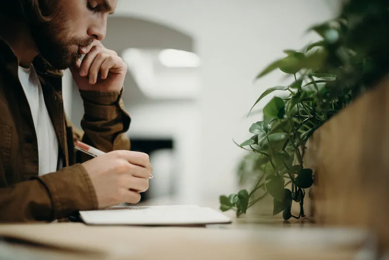 A man resting his chin on his hand while writing notes at a desk