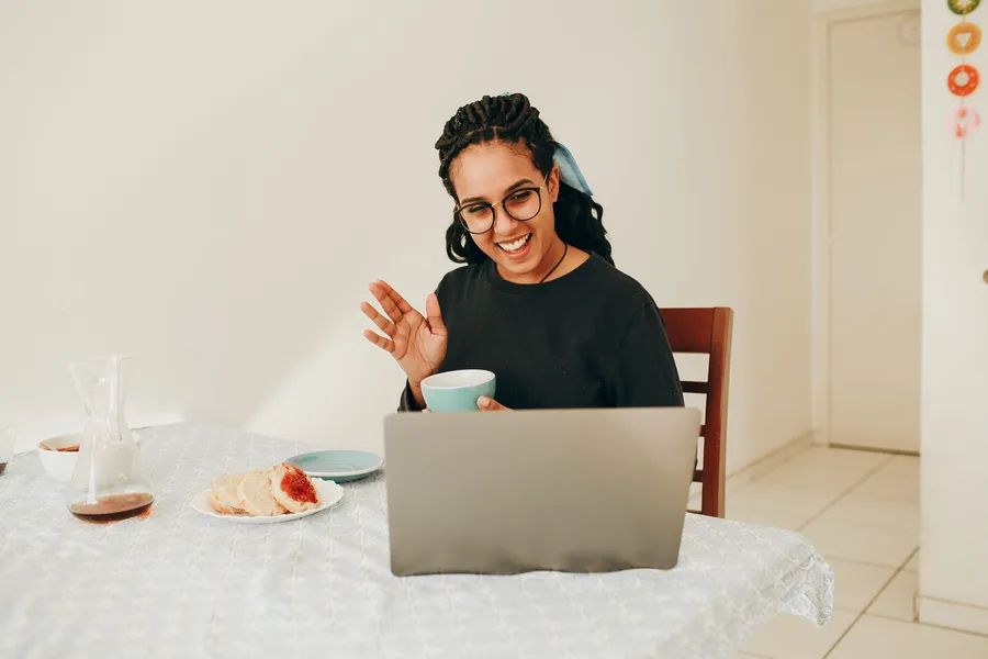 A woman waving to someone on a laptop video call at home