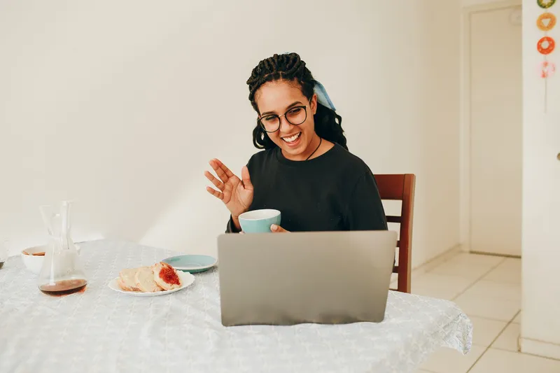A woman waving to someone on a laptop video call at home