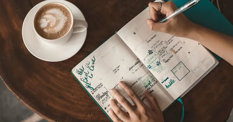 Hands writing in a weekly planner beside a cup of coffee