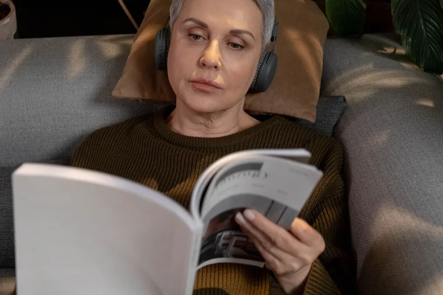 A woman wearing headphones reading a magazine on a sofa