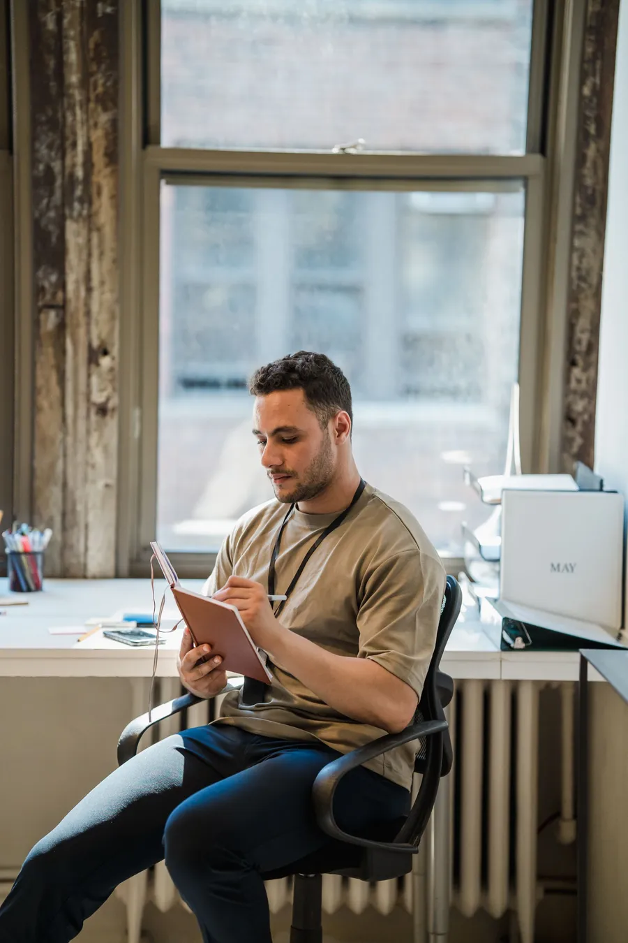 A man reading his notes while sitting at a desk by a window