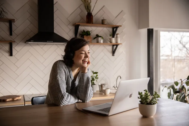 A woman smiling in her kitchen in front of a laptop