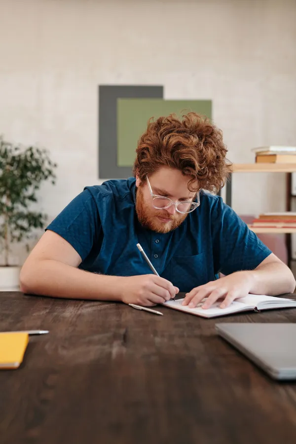 A man writing notes in a notebook at a wooden table